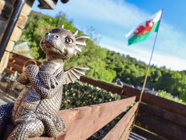 A small dragon statue on a wooden fence with a Welsh flag and trees in the background at Glyndwr in Betws-Y-Coed