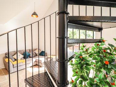 A black metal spiral staircase with a plant nearby and a gray sofa with cushions in a living room at Glyndwr in Betws-Y-Coed