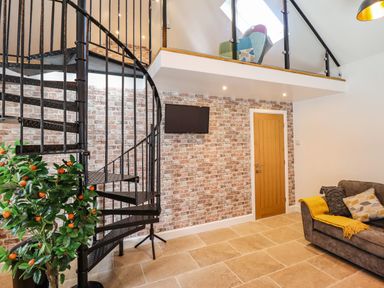 A living area with a black spiral staircase a sofa with cushions and a yellow throw a brick wall with a door and a wall-mounted TV at Glyndwr in Betws-Y-Coed