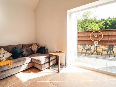 A corner sofa with cushions and a small table next to an open door leading to an outdoor seating area with two chairs and a table at Glyndwr in Betws Y Coed
