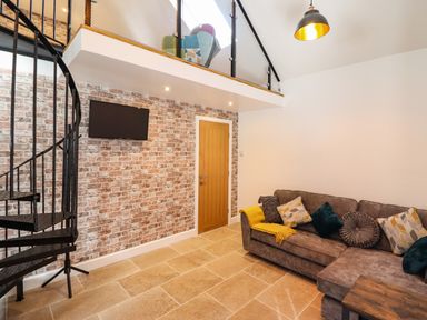 A living room with a sectional sofa and spiral staircase at Glyndwr in Betws-Y-Coed