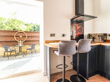 A kitchen corner with two bar stools a wooden countertop and a glass door leading to a patio with a table and two chairs at Glyndwr in Betws-Y-Coed