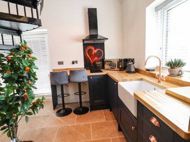 A kitchen with a wooden countertop a white sink two gray bar stools and a small plant by the window at Glyndwr in Betws-Y-Coed