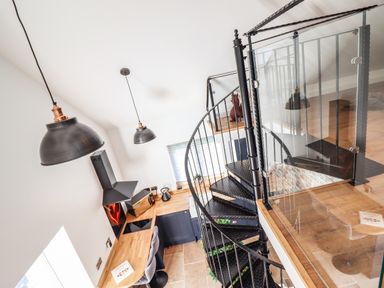 A kitchen area with a wooden countertop black cabinets black spiral staircase and pendant lights at Glyndwr in Betws-Y-Coed