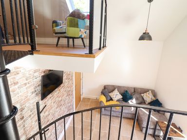 A two-level living room with a spiral staircase a gray corner sofa with cushions a wall-mounted TV and a multicolored armchair at Glyndwr in Betws-Y-Coed