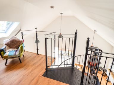 An upstairs area with a spiral staircase a patterned armchair and wooden flooring at Glyndwr in Betws-Y-Coed