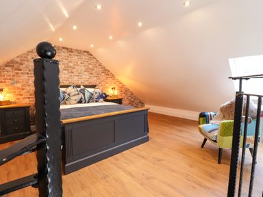 A bedroom with a bed and pillows against a brick wall and a colorful chair near a skylight at Glyndwr in Betws Y Coed