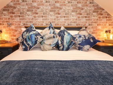 A bed with four decorative pillows with bird designs a blue blanket and exposed brick wall at Glyndwr in Betws-Y-Coed
