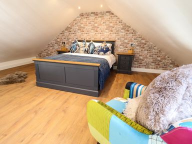 A bedroom with a double bed and bedside tables against a brick wall and a colorful armchair at Glyndwr in Betws Y Coed