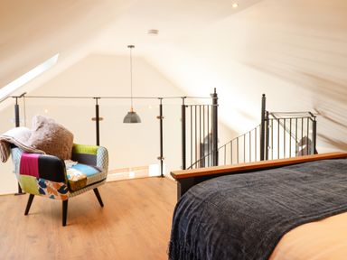 An attic bedroom with a bed covered by a dark blanket and a colorful armchair with a throw at Glyndwr in Betws-Y-Coed