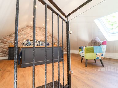 A bedroom with a dark bed frame and pillows a colorful armchair next to a skylight window and a brick wall at Glyndwr in Betws-Y-Coed