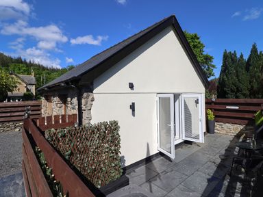 A small building with white doors opening onto a stone patio with outdoor furniture at Glyndwr in Betws-Y-Coed
