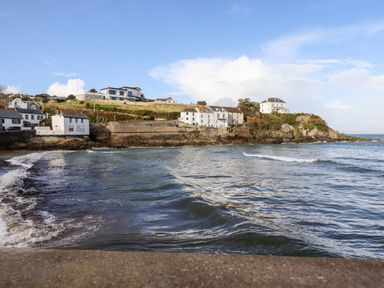 A coastal scene with houses on a rocky shoreline and waves in the sea at EdyVean in Portmellon near Mevagissey