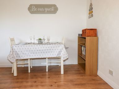 A dining area with a table covered by a cloth and two chairs next to a wooden bookshelf at EdyVean in Portmellon near Mevagissey