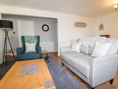 A living room with a blue armchair grey sofa wooden coffee table and a floor lamp at EdyVean Portmellon near Mevagissey