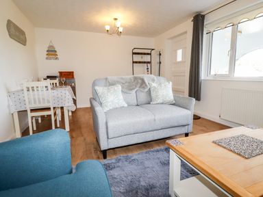 A living room with a grey loveseat two cushions a blue armchair a wooden coffee table and a dining table with chairs at EdyVean in Portmellon near Mevagissey