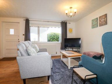A living room with a grey sofa blue armchair wooden coffee table and television at EdyVean in Portmellon near Mevagissey