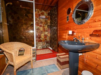A bathroom with a stone walk-in shower a wicker chair a dark sink a round mirror and wooden walls at EdyVean Portmellon near Mevagissey