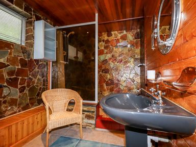 A bathroom with a shower area a wicker chair a gray sink and wooden and stone walls at EdyVean Portmellon near Mevagissey