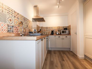 A kitchen with patterned tiled backsplash wooden countertops gray cabinets and appliances at EdyVean Portmellon near Mevagissey