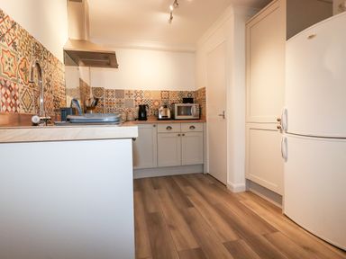 A kitchen with patterned tile backsplash wooden countertops white cabinets and appliances at EdyVean Portmellon near Mevagissey