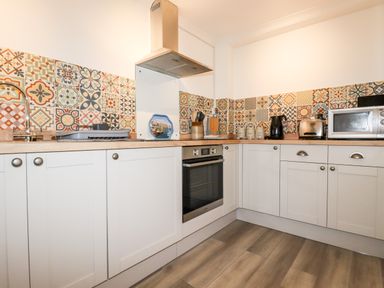 A kitchen with patterned tile backsplash white cabinets wooden countertop and appliances at EdyVean Portmellon near Mevagissey