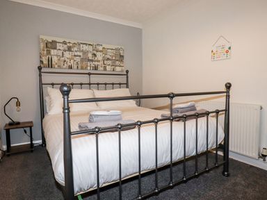 A bedroom with a metal bed frame white bedding folded towels bedside table with lamp and wall art at EdyVean Portmellon near Mevagissey