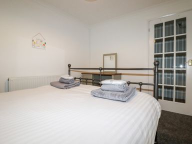 A bedroom with a metal bed frame white bedding folded towels a mirror on a wooden dresser and a white door with glass panels at EdyVean in Portmellon near Mevagissey