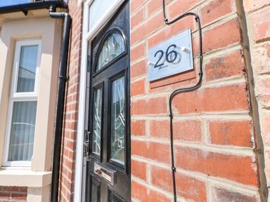 A black front door with decorative glass panels and a house number 26 on a red brick wall at Lobster Pot Retreat in Newbiggin-By-The-Sea