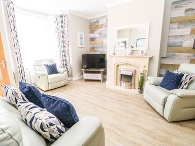 A living room with cream leather sofas and armchairs a fireplace and a television at Lobster Pot Retreat in Newbiggin-By-The-Sea