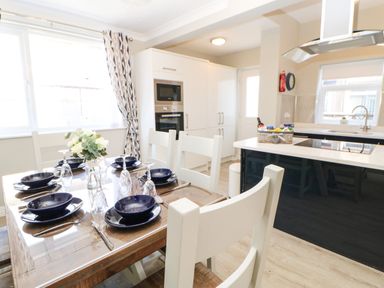 A dining table set with plates and glasses next to a kitchen with white cabinets and an island at Lobster Pot Retreat in Newbiggin-By-The-Sea