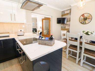 A kitchen with a cooking island a wicker basket on the counter and a dining table with chairs and a wall clock at Lobster Pot Retreat in Newbiggin-By-The-Sea