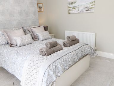 A bedroom with a bed with patterned bedding and pillows and two sets of rolled towels on the bed at Lobster Pot Retreat in Newbiggin By The Sea