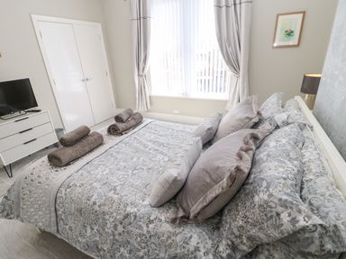A bedroom with a bed covered with patterned bedding and pillows and rolled towels placed on top at Lobster Pot Retreat in Newbiggin-By-The-Sea