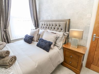 A bedroom with a bed with multiple pillows and a wooden bedside table with a lamp at Lobster Pot Retreat in Newbiggin-By-The-Sea