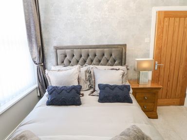 A bedroom with a bed with pillows beside a wooden nightstand with a lamp at Lobster Pot Retreat in Newbiggin-By-The-Sea
