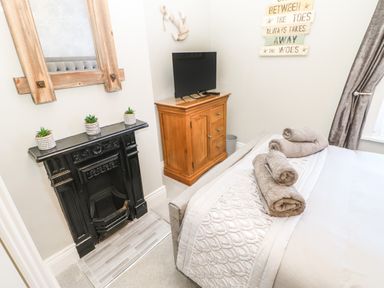 A bedroom with a bed holding rolled towels a wooden dresser with a TV and a black decorative fireplace at Lobster Pot Retreat in Newbiggin-By-The-Sea