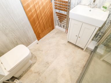 A bathroom with a toilet a wooden door a white sink with cabinet and a heated towel rail at Lobster Pot Retreat in Newbiggin-By-The-Sea