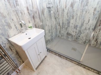A bathroom with a white sink cabinet and a shower area with rustic wood patterned walls at Lobster Pot Retreat in Newbiggin-By-The-Sea
