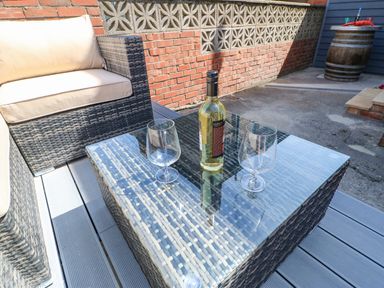An outdoor seating area with a wicker sofa and glass table with a bottle and two glasses at Lobster Pot Retreat in Newbiggin-By-The-Sea