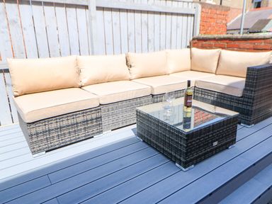 An outdoor seating area with a wicker sofa set and a matching coffee table with a bottle and two wine glasses on the table at Lobster Pot Retreat in Newbiggin By The Sea