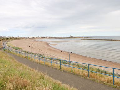A beach with sand and waves near a path with blue railings at Lobster Pot Retreat in Newbiggin-By-The-Sea