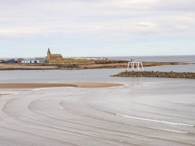 A coastal view with a beach a stone jetty and a church in the background at Lobster Pot Retreat in Newbiggin-By-The-Sea