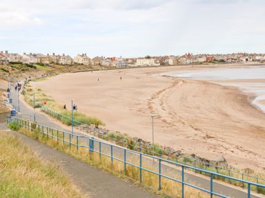 A view of a sandy beach with a walkway and railings along the side and houses in the background at Lobster Pot Retreat in Newbiggin-By-The-Sea