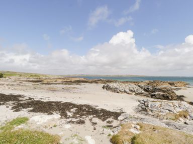 A sandy beach with seaweed and rocks under a partly cloudy sky at Ti Tom Narta in Trabane near Lettermore County Galway