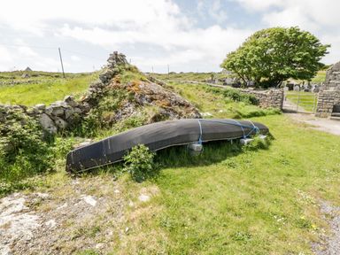 An upside down black boat tied with blue ropes resting on grass near a stone wall with a gate and a tree at Ti Tom Narta in Trabane near Lettermore County Galway