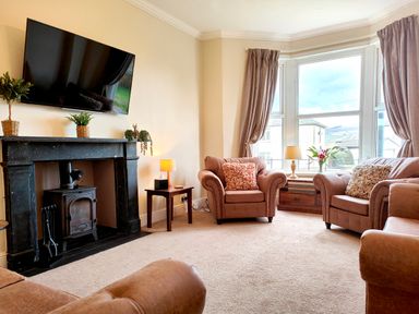 A living room with brown armchairs a fireplace with plants and a wall-mounted tv at Grove House in Egremont