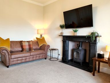 A living room with a brown sofa and pillows next to a fireplace with a TV above at Grove House in Egremont
