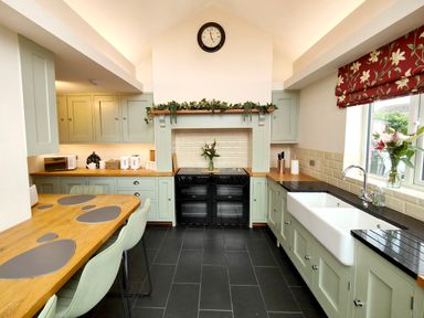 A kitchen with light green cabinets black oven wooden countertops and a dining table at Grove House in Egremont