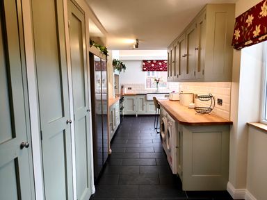 A galley kitchen with cupboards appliances and a window with red floral blinds at Grove House in Egremont
